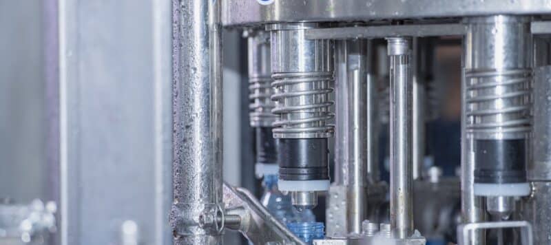 Close-up of a stainless steel industrial bottle-filling machine in a commercial water system filling plastic bottles.