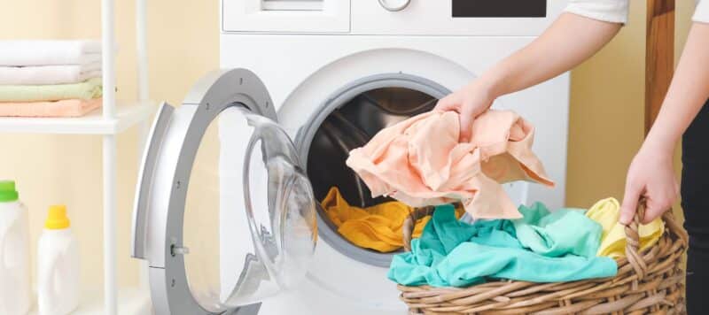 person doing laundry and putting clothes into the machine