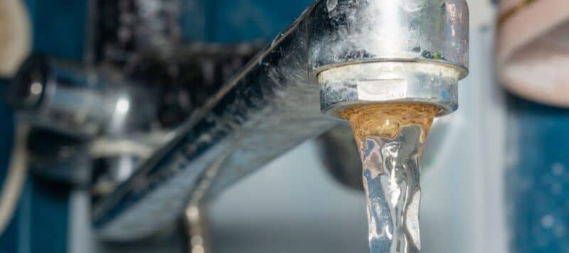 A metal kitchen faucet dispensing discolored, rusty-looking water.