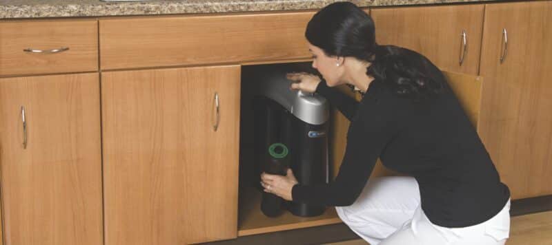 A woman installs a water filtration system under a kitchen sink