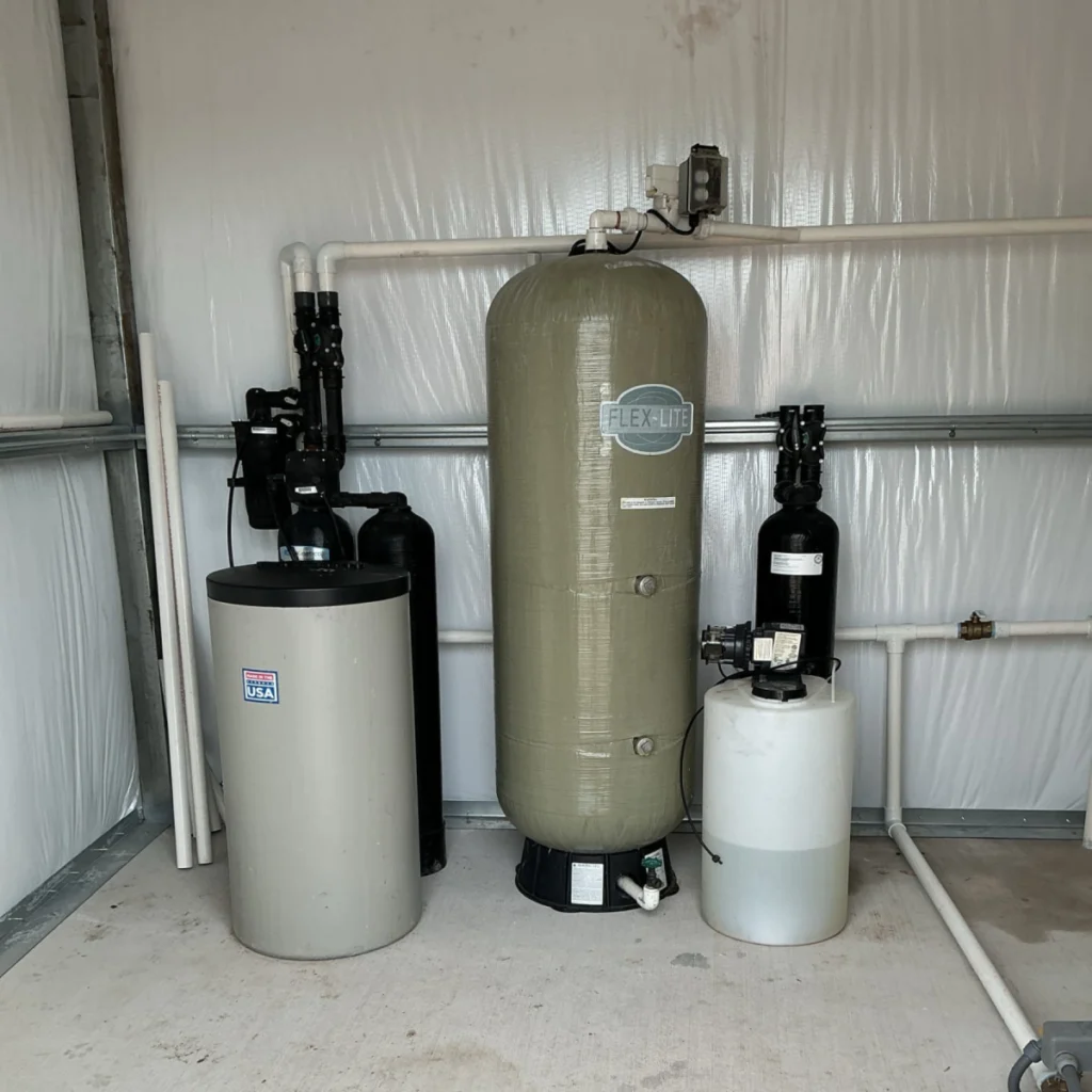 Water treatment system with a large Flex-Lite pressure tank, two smaller tanks, and connected PVC piping.
