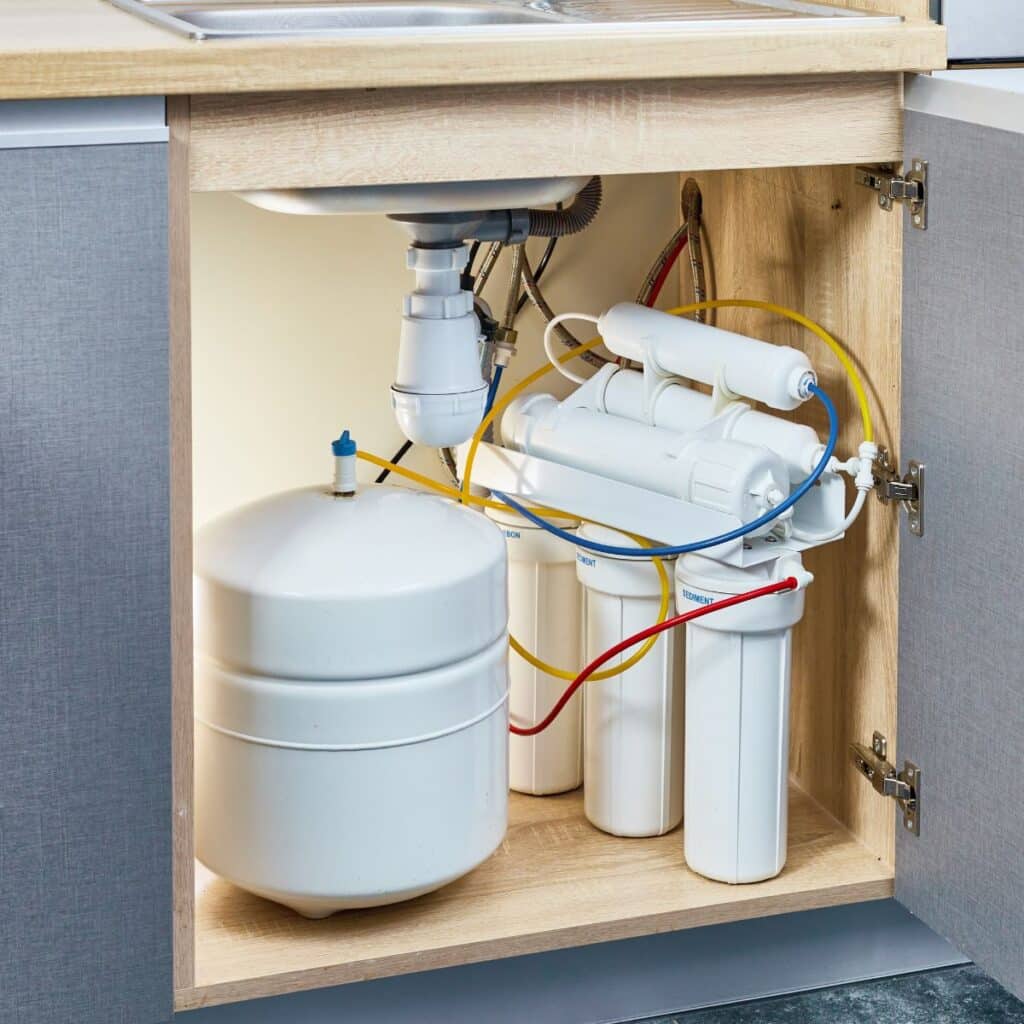 A multi-stage water filtration system with a white storage tank installed under a kitchen sink, as seen in our frequently asked questions.