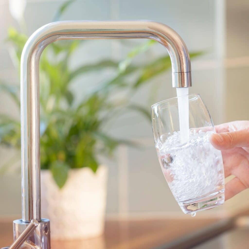 A hand holds a glass under a kitchen faucet as water fills it, a common sight for those browsing our frequently asked questions.