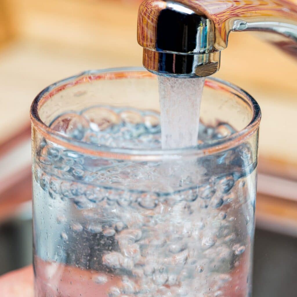 Water flows from a faucet into a clear glass, a common sight often addressed in frequently asked questions.