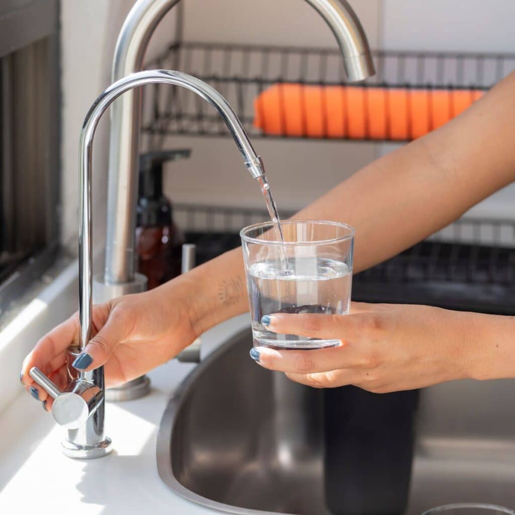 A person fills a glass with water from a kitchen faucet, a common scenario often addressed in our frequently asked questions.