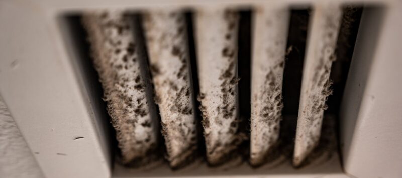 A close-up of a dirty air vent with thick layers of dust and debris buildup on the slats.