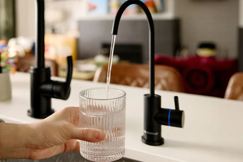 A hand holds a glass under a black reverse osmosis system faucet as water flows into it.